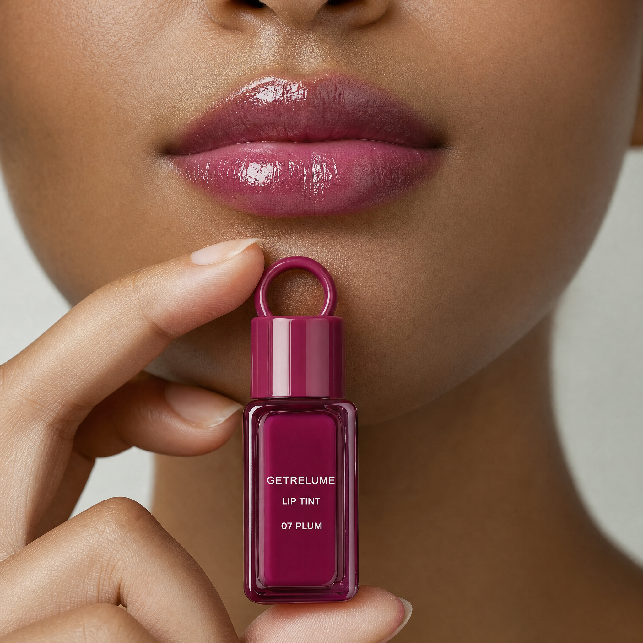 Model wearing glossy plum lip tint and holding RELUME Juicy Lip Tint