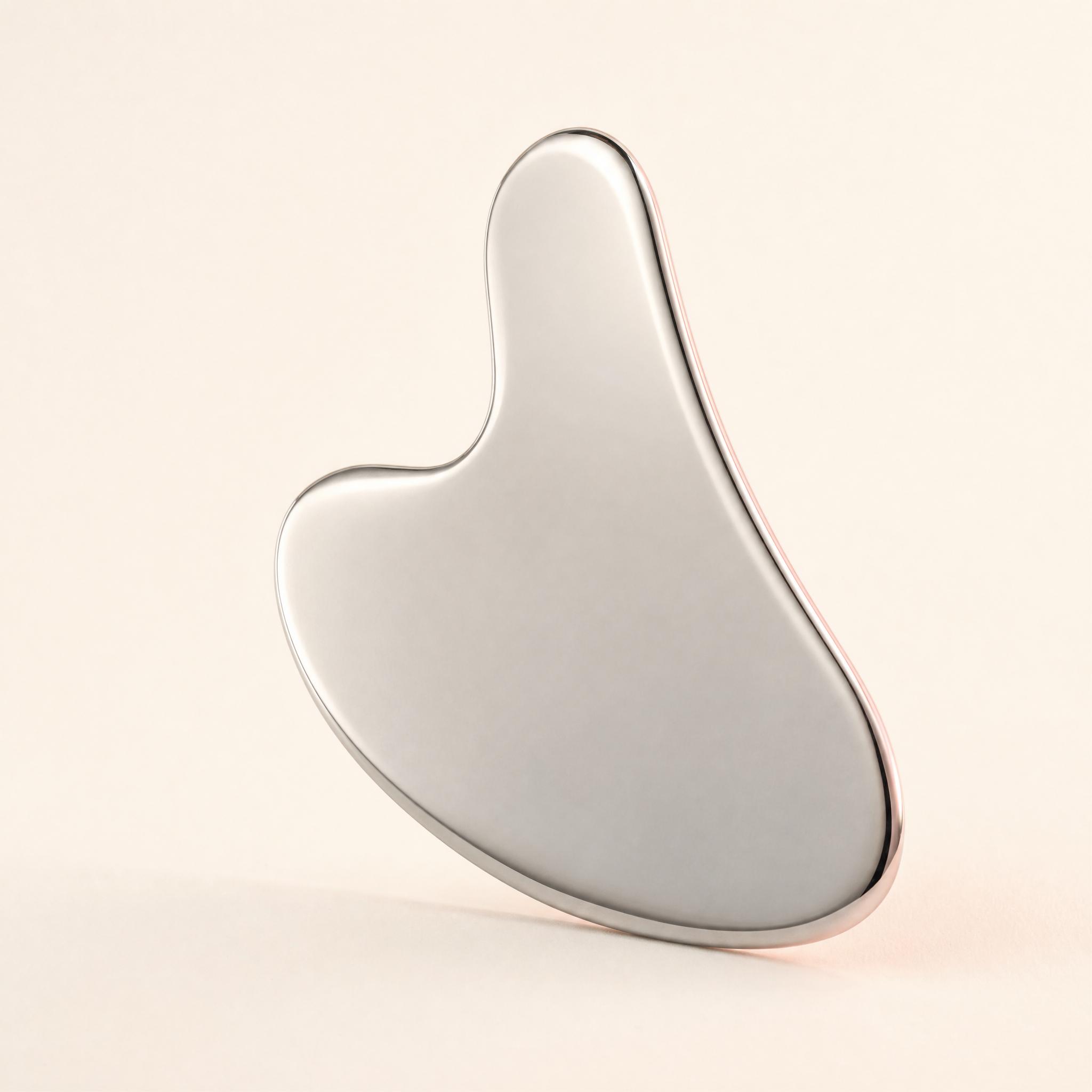 Polished stainless-steel gua sha on a warm ivory background
