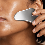 Woman gently using a stainless-steel gua sha along her cheek