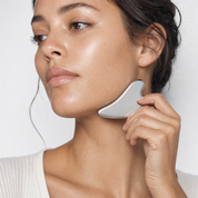 Woman using a stainless-steel gua sha along her jawline